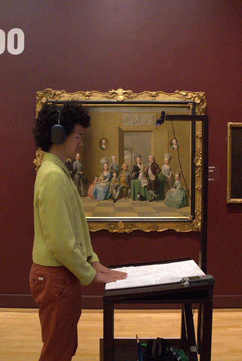 A visitor with headphones rests both hands on a white relief in front of an 18th-century family portrait at the National Gallery of Denmark, with a camera mounted above the relief